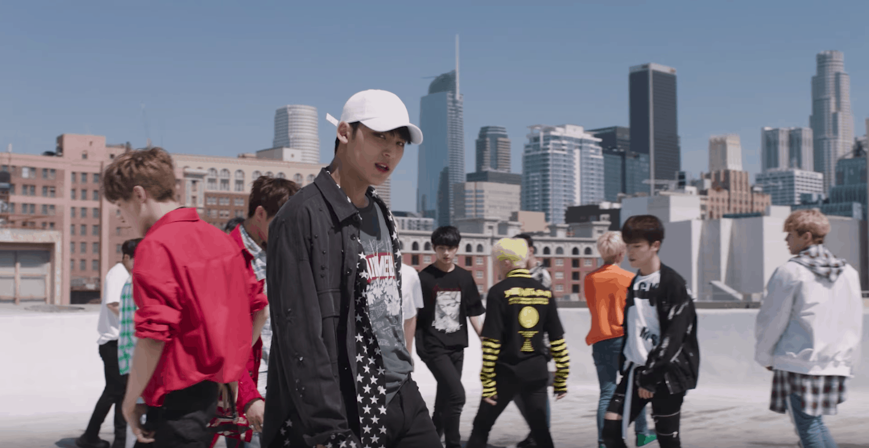 Seventeen kpop fashion: Member wearing a white baseball hat, graphic tee shirt, patterned button-down and gray jacket