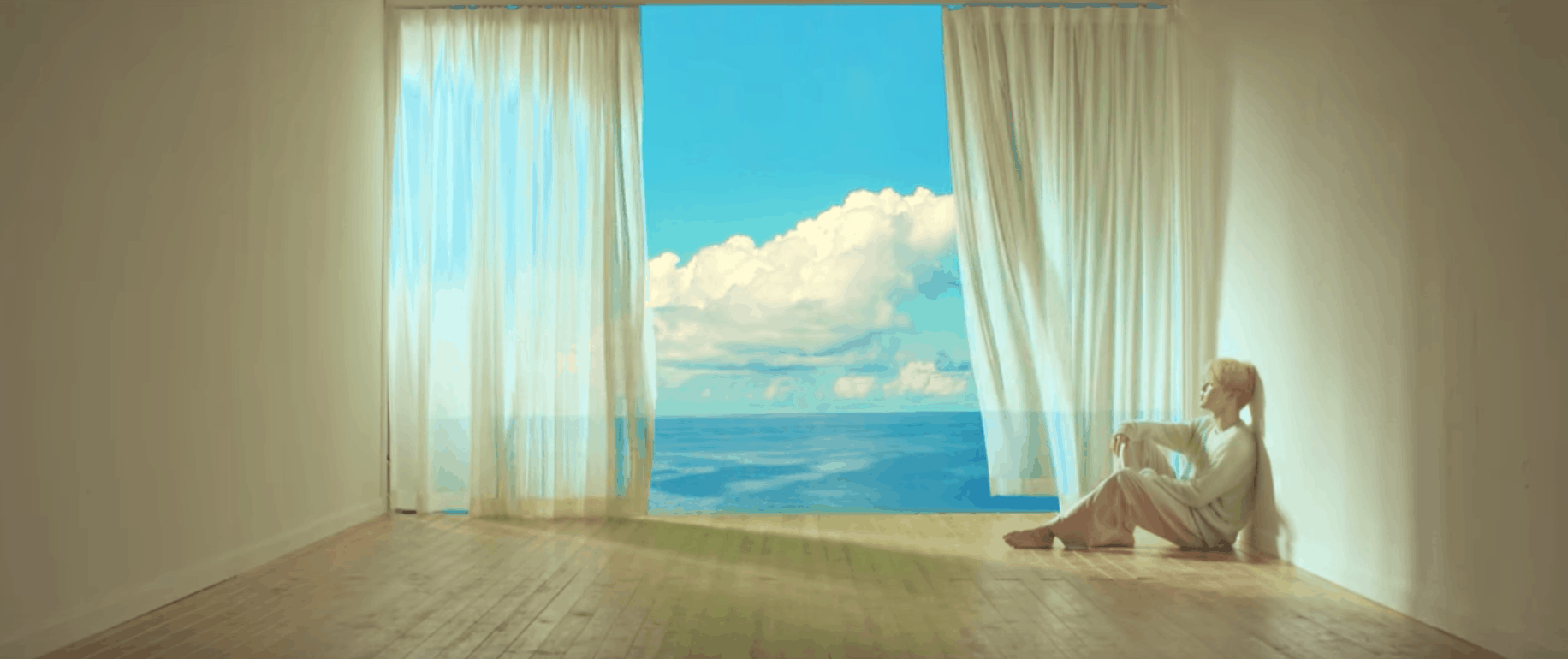 BTS Serendipity music video: Shot of the lead singer sitting on the floor in a room next to a big open window overlooking the ocean