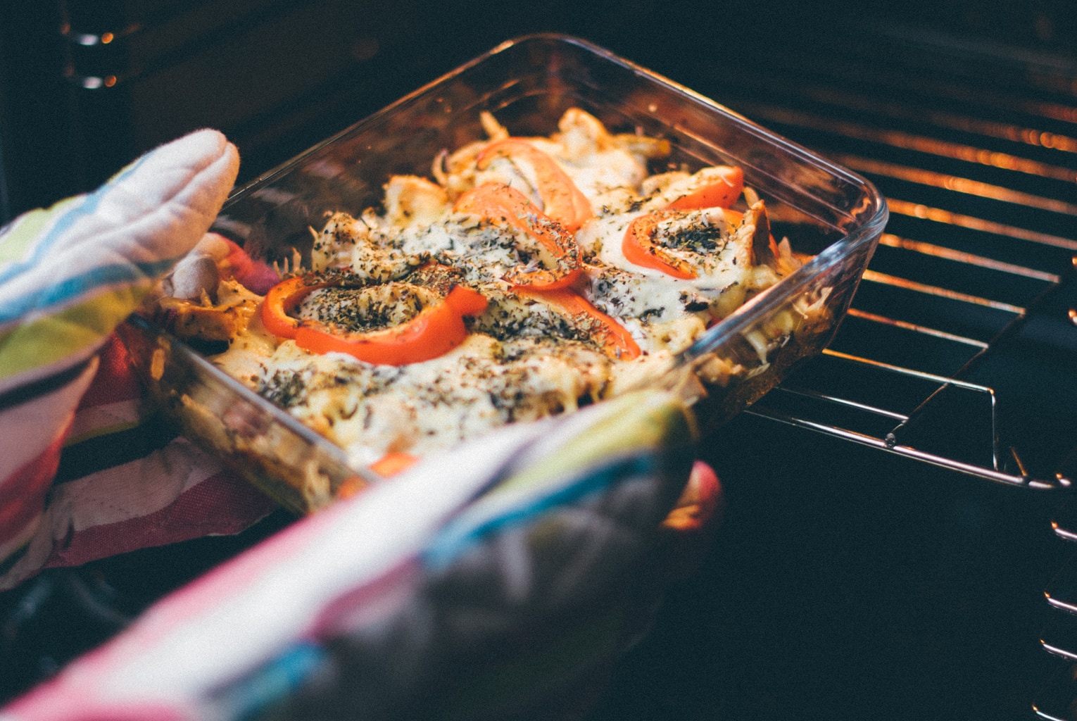 Person holding food with oven mitts putting food in oven