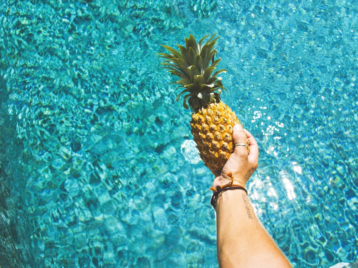 Person holding a pineapple over a pool