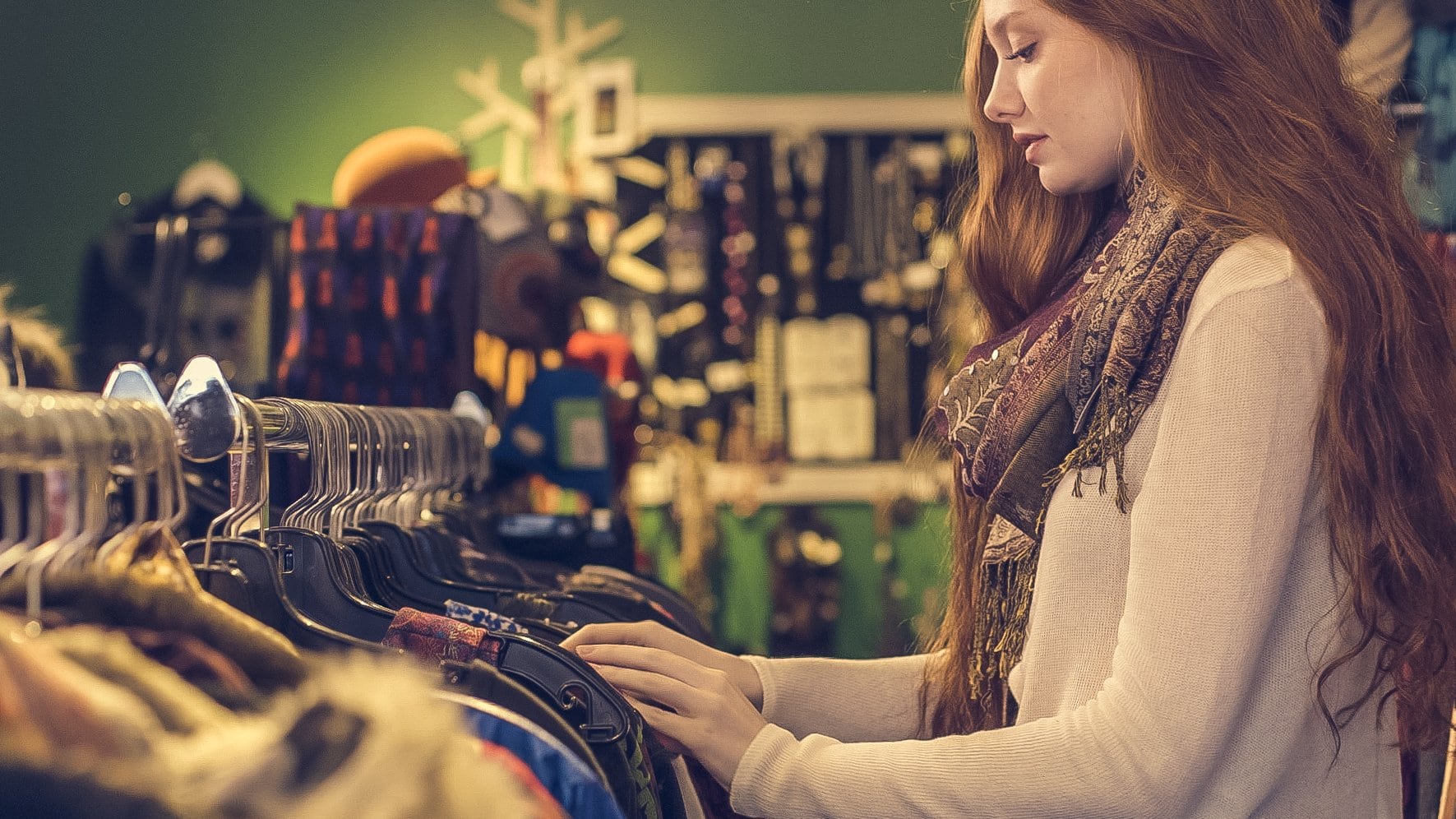 Photo of a red headed girl wearing a scarf and sweater shopping at a thrift store.