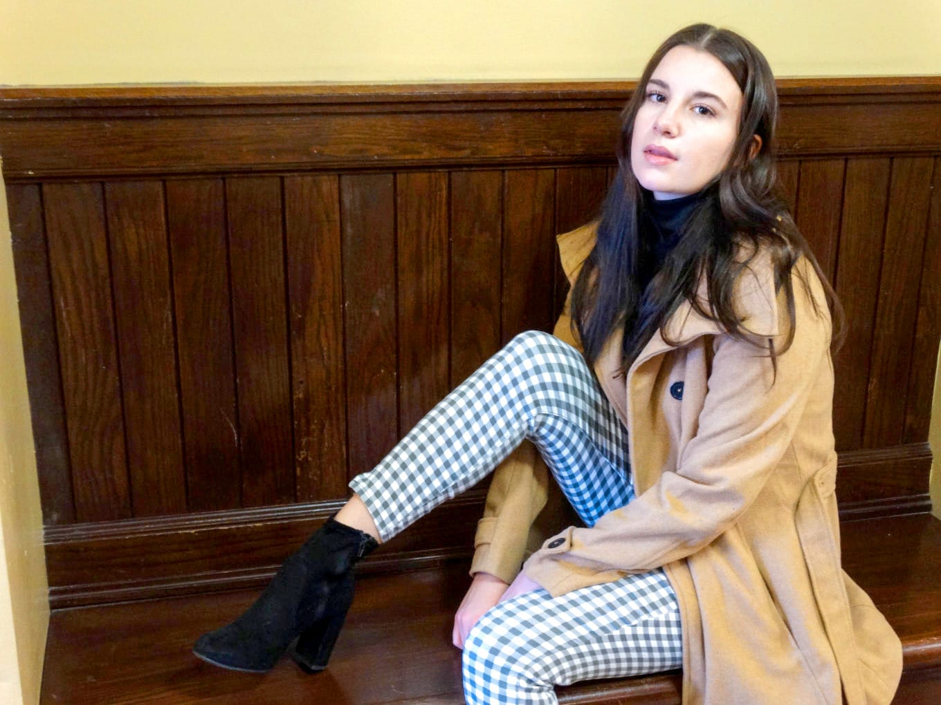 Ariel pairs her checkered pants with black booties and a long camel trench coat.