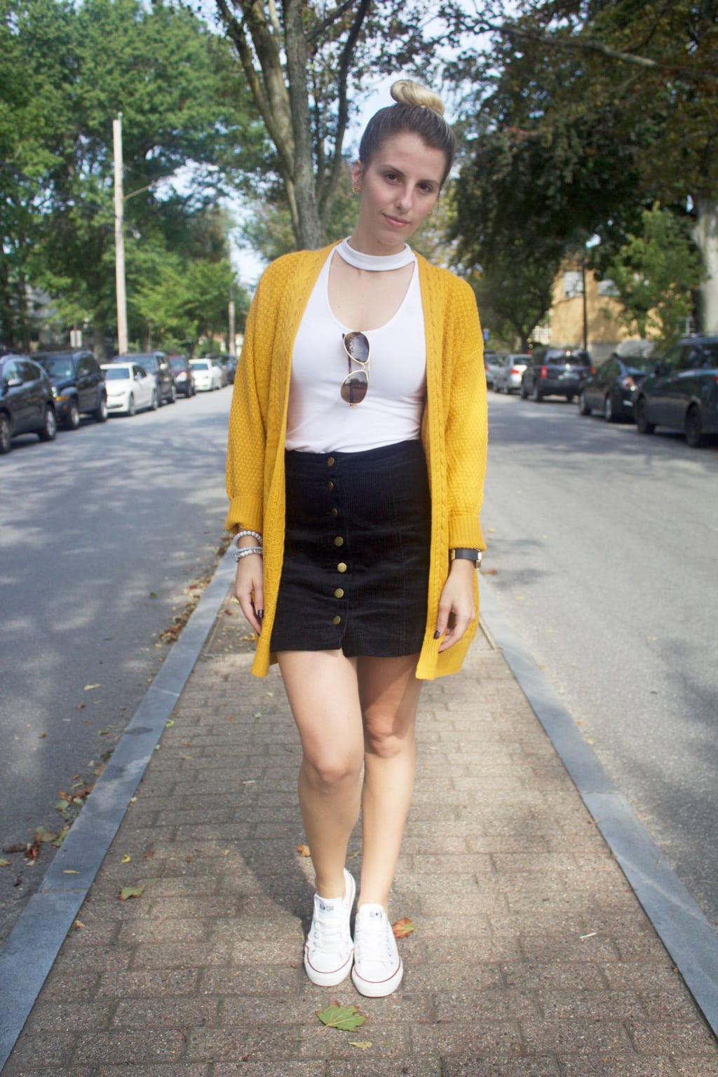 Casual student style: University of Bridgeport student Jessica wears a white top with a chunky mustard cardigan, navy button-up miniskirt, and white Converse sneakers. She tops off her look with some simple aviators and a topknot.