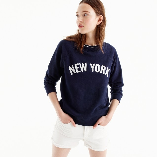Photo of model wearing navy blue graphic sweatshirt with "NEW YORK" across the chest in white with white shorts