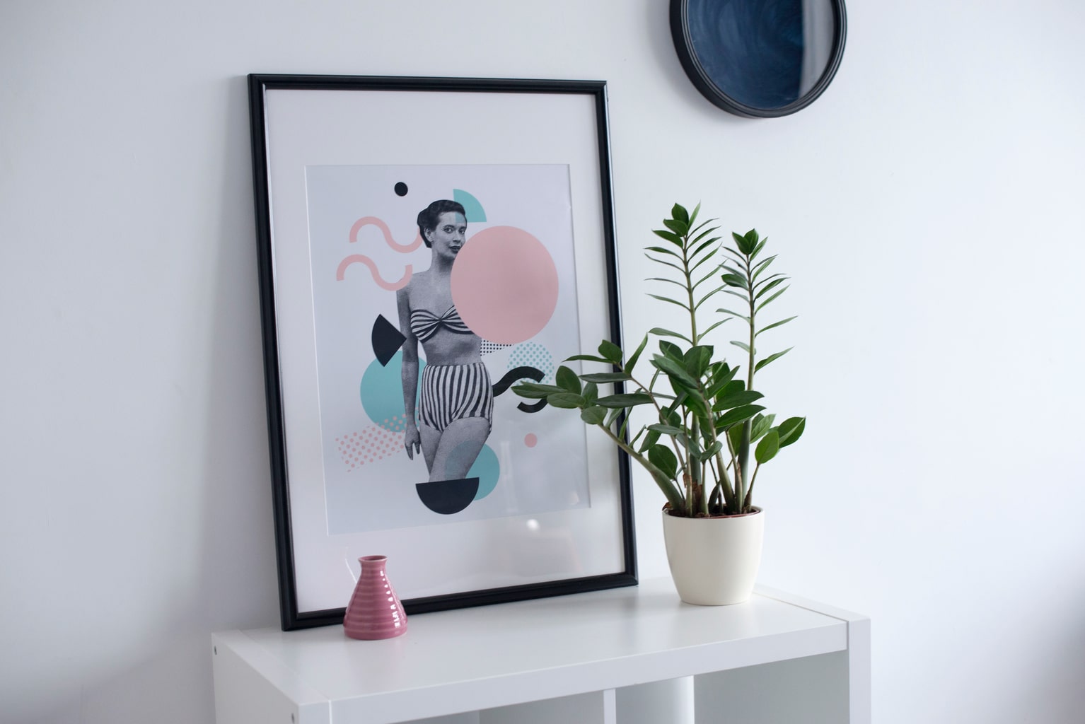 White bookcase with a framed print on top in a white apartment