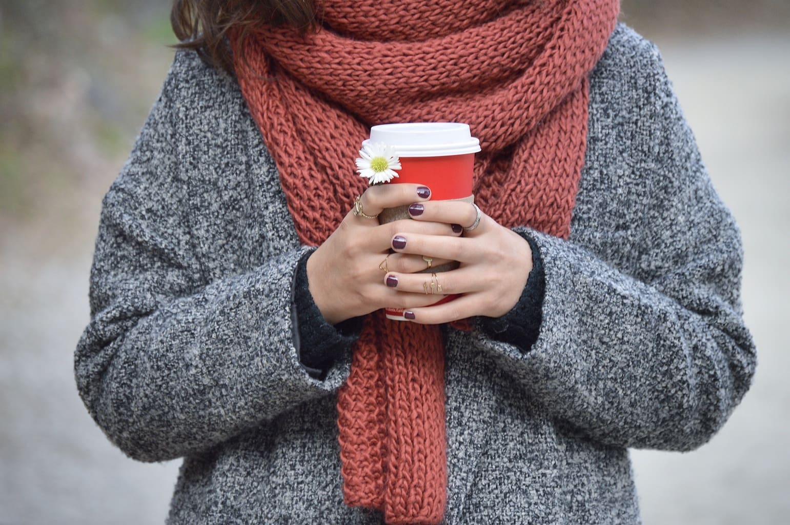 Girl holding holiday Starbucks coffee in winter, wearing grey knit coat and red scarf