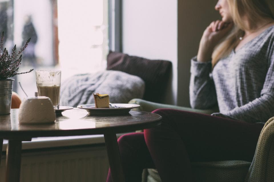 Woman looking out window in cafe with cake and coffee