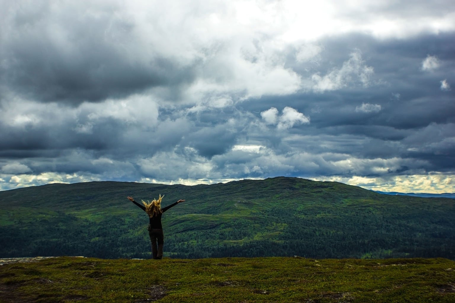 Woman on a hilltop with her arms outstretched under a cloudy sky