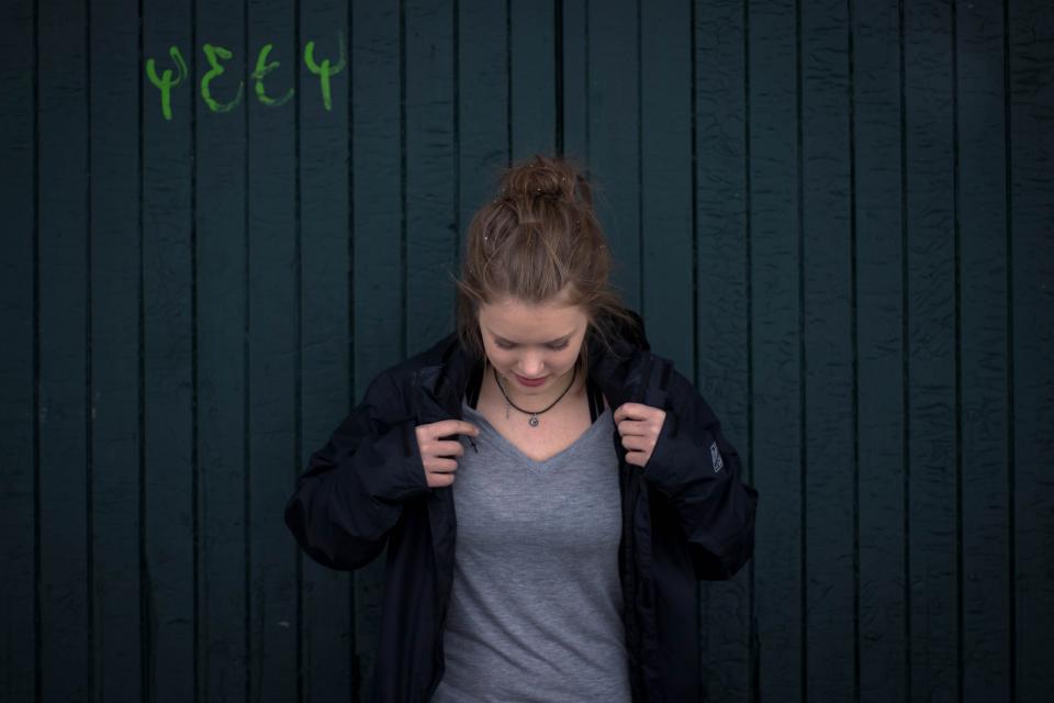 Woman against dark wall in grey t-shirt and black jacket