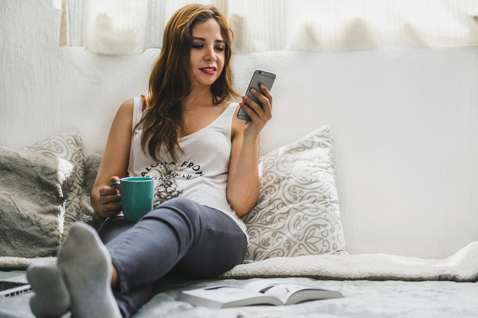 Woman sitting in bed with a mug and her phone