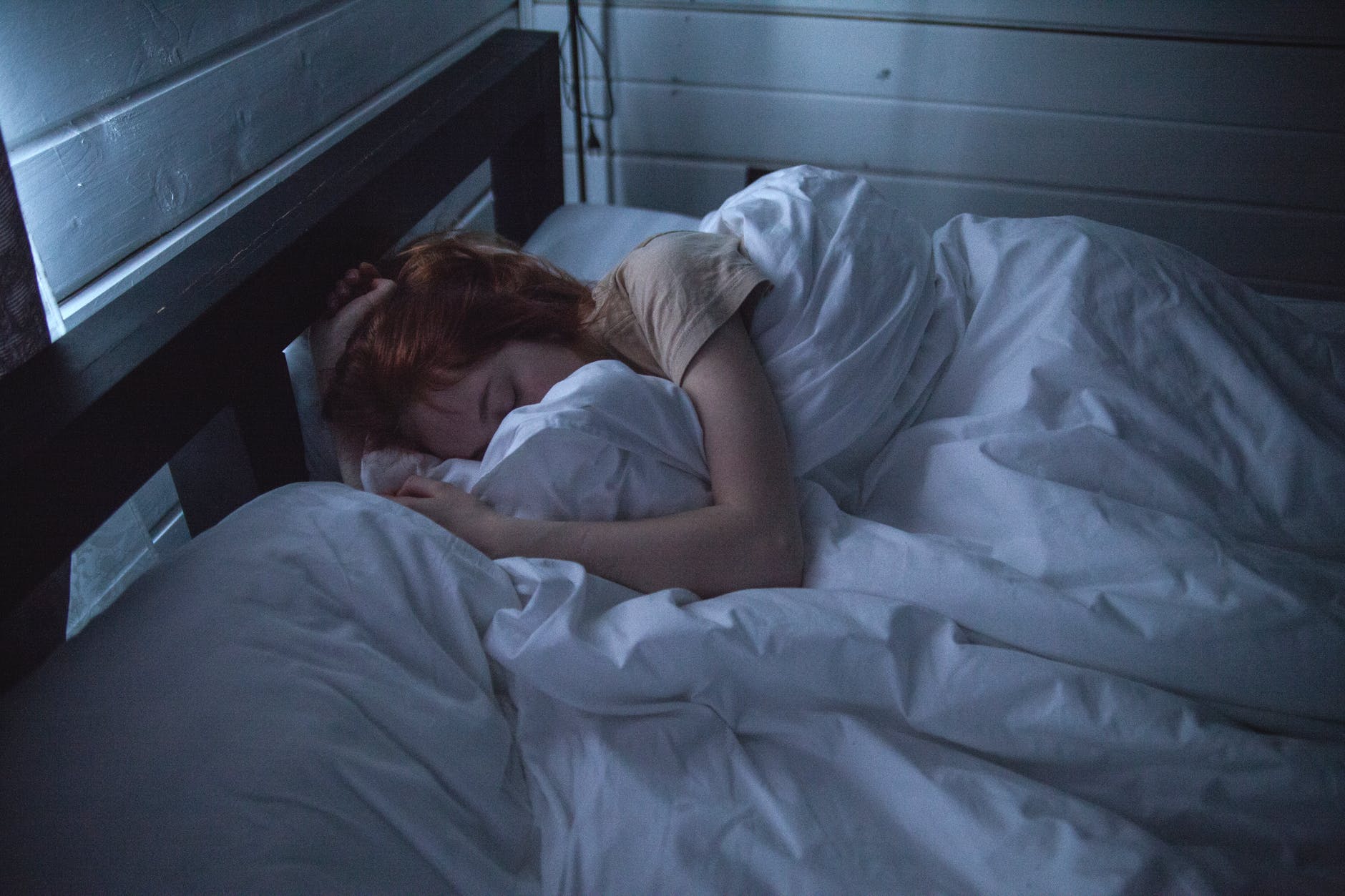 Girl with red hair asleep in a bed with white comforter