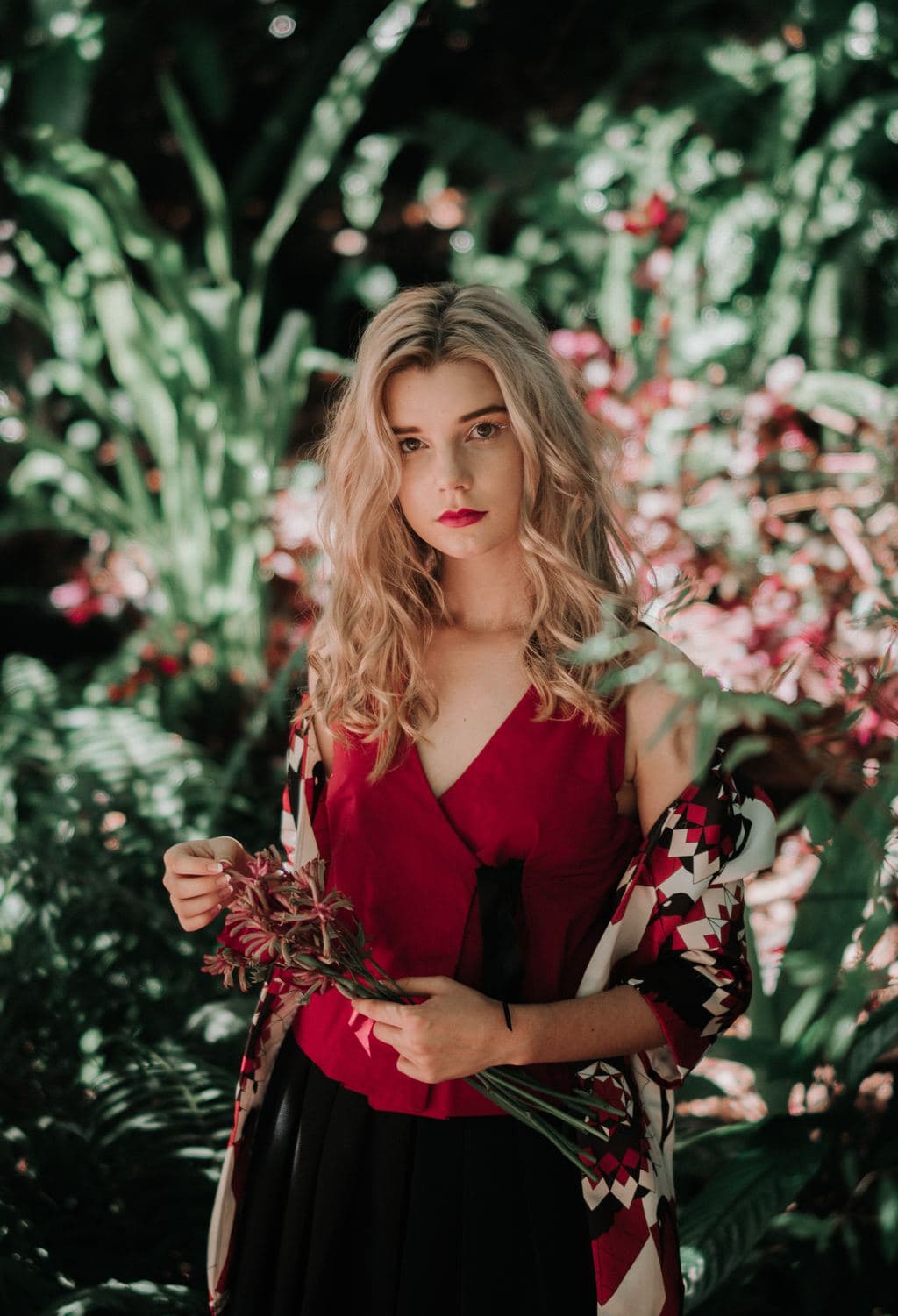 Woman clad in burgundy kimono and top holding flowers.