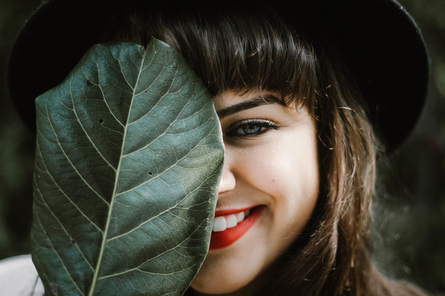 Woman wearing red lipstick and covering half of her face with a leaf