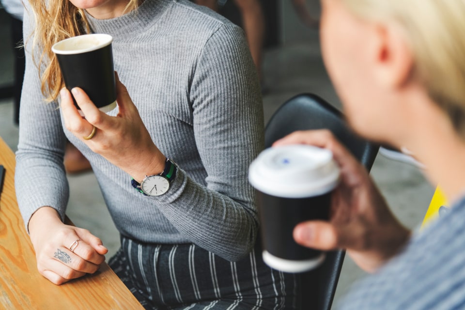 Woman with striped pants drinking coffee in a cafe with friend