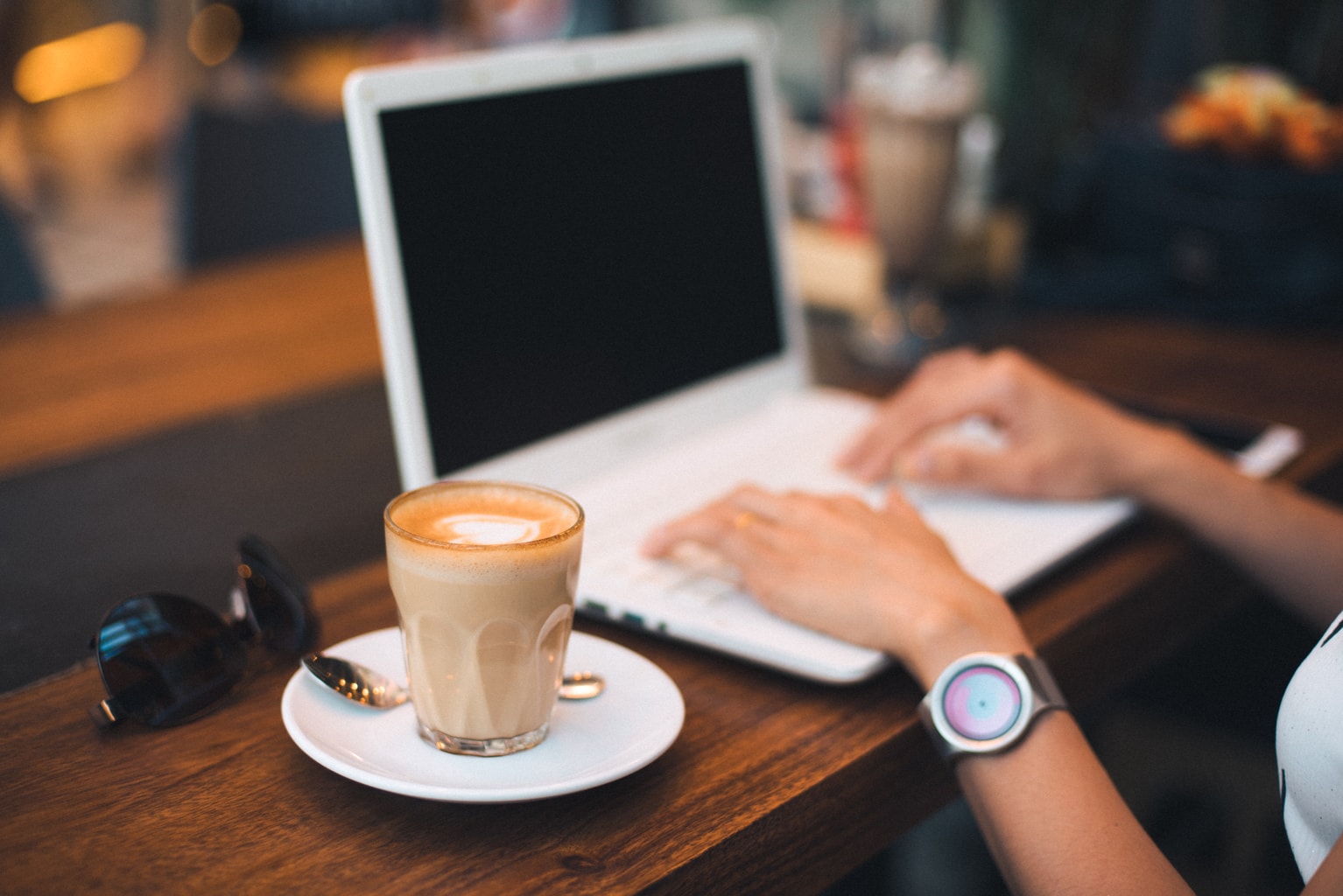 Girl wearing a watch working on a computer with a coffee next to her.