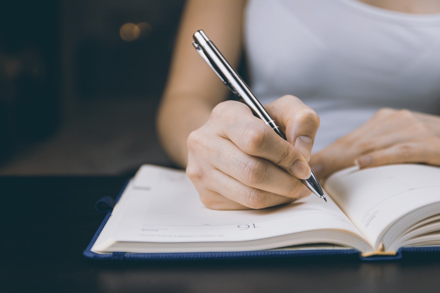 A woman writing in a notebook with a pen.