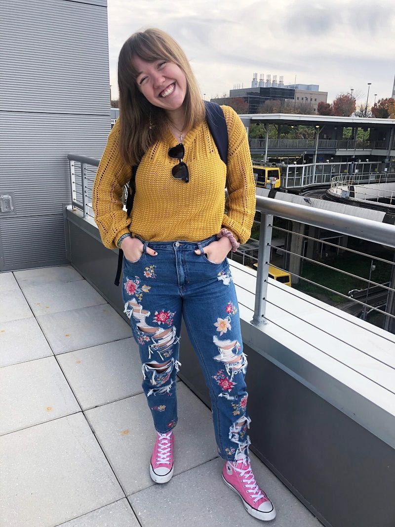 West Virginia University student Maria wears a chunky mustard knit sweater, floral embroidered and ripped jeans, and high-top pink Converse sneakers.