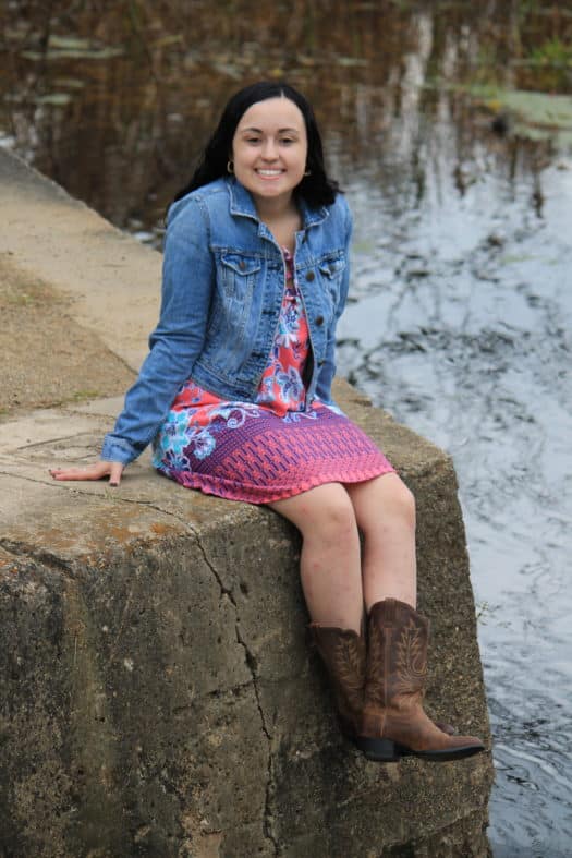 GVSU student Abbey wears a coral, pink, and purple summer dress with a medium-wash jean jacket and cowboy boots.