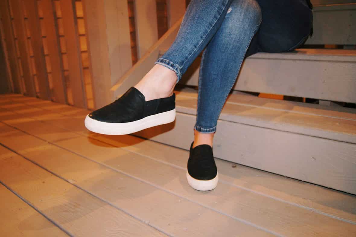 Renee wears black-slip-ons with large white soles and skinny faded jeans.