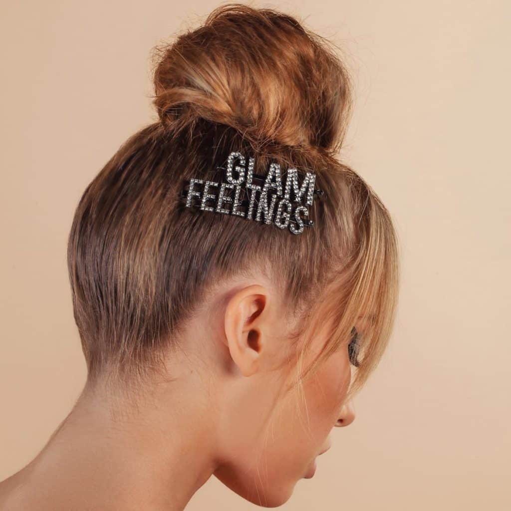 Spring 2019 accessory trends: Close-up side view of woman with a topknot wearing embellished GLAM and FEELINGS hair clips