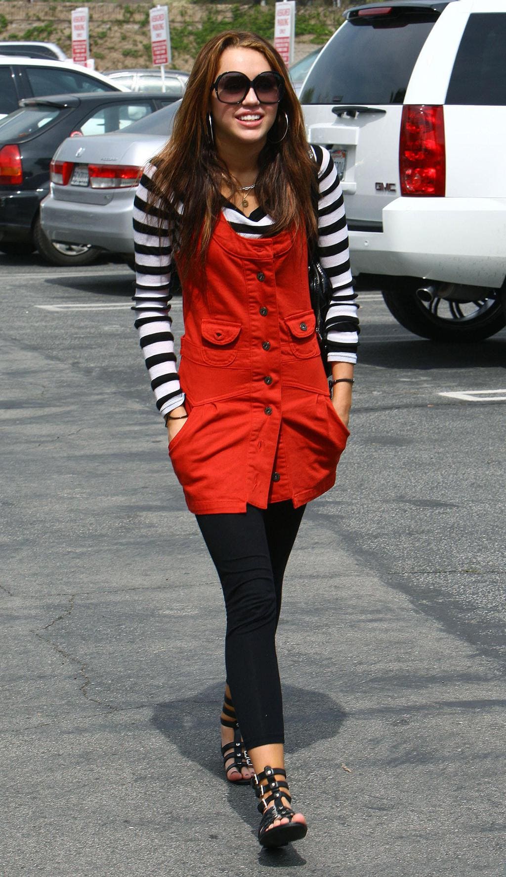 miley cyrus walking in a jumper dress, long sleeve striped tee shirt, leggings, and gladiator sandals
