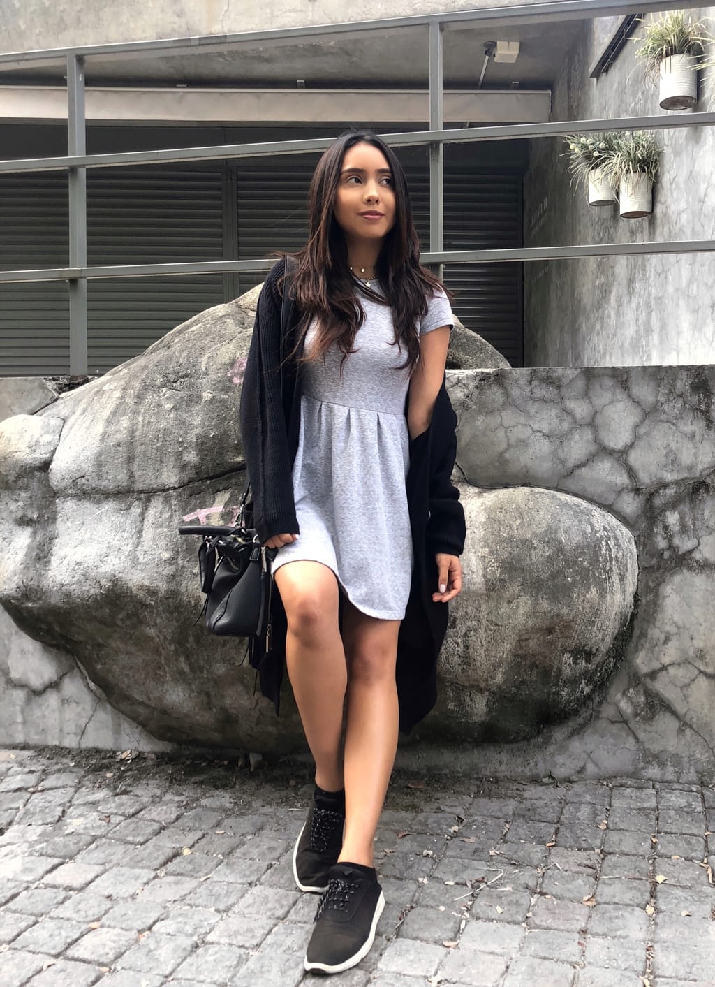 Cynthia wears a simple, grey, knit mini dress with a long, black Free People cardigan, and casual sneakers.