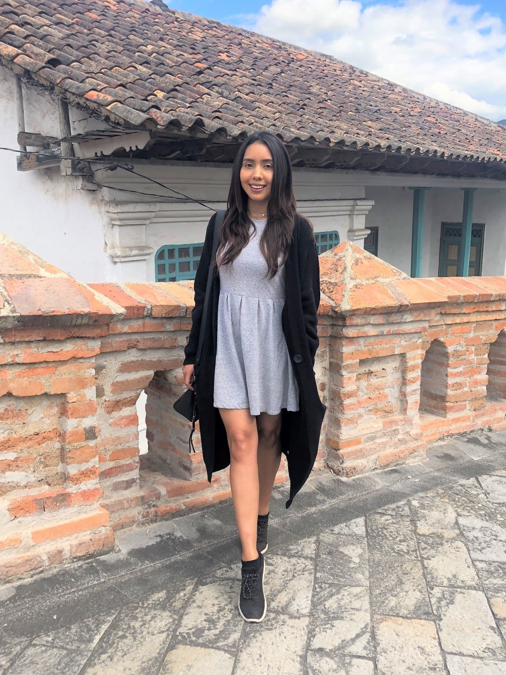 Cynthia wears a grey knit dress with a long, black cardigan, with black sneakers.