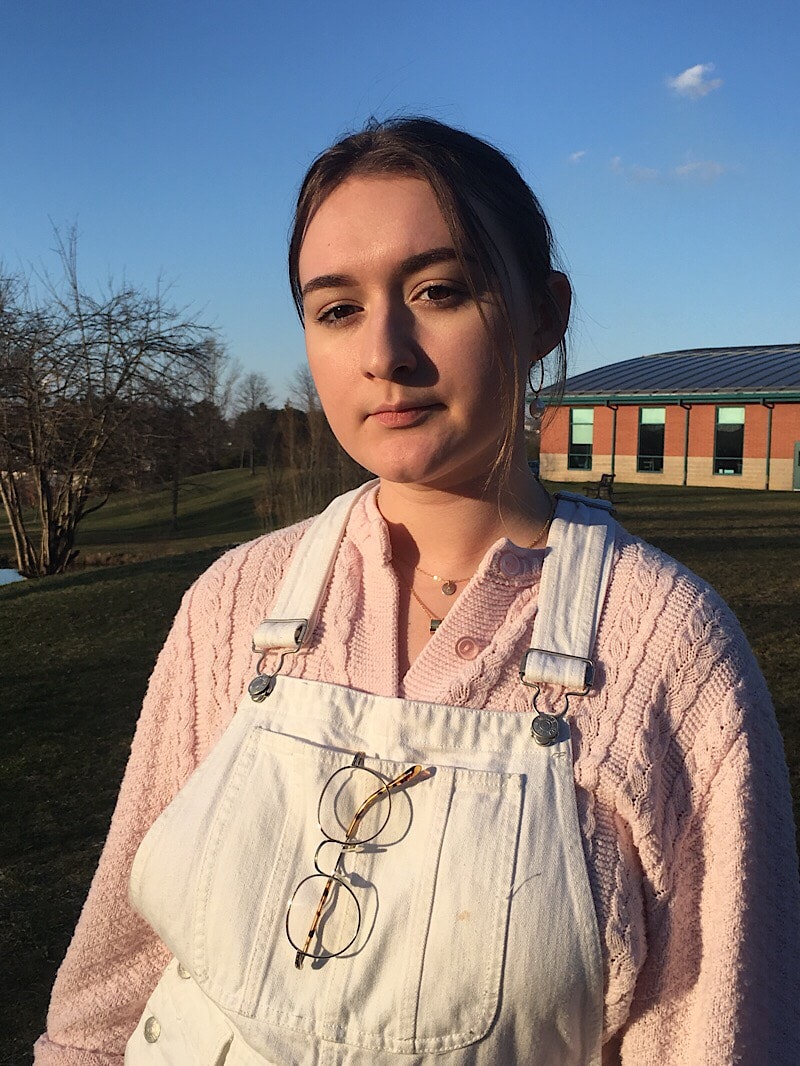 Abby wears a chunky cable-knit baby pink sweater with white denim overalls.