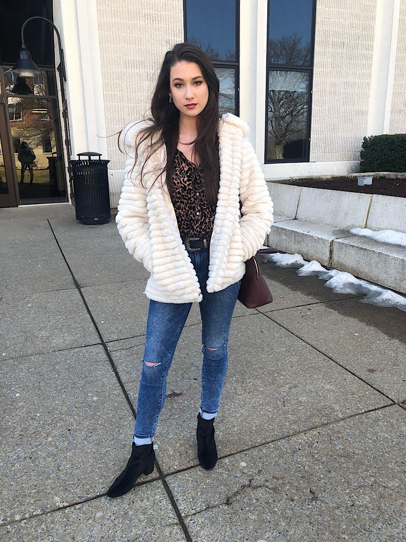 Bella wears a leopard print button-up shirt tucked into medium-wash cuffed skinny jeans, black boots, and a white furry coat.