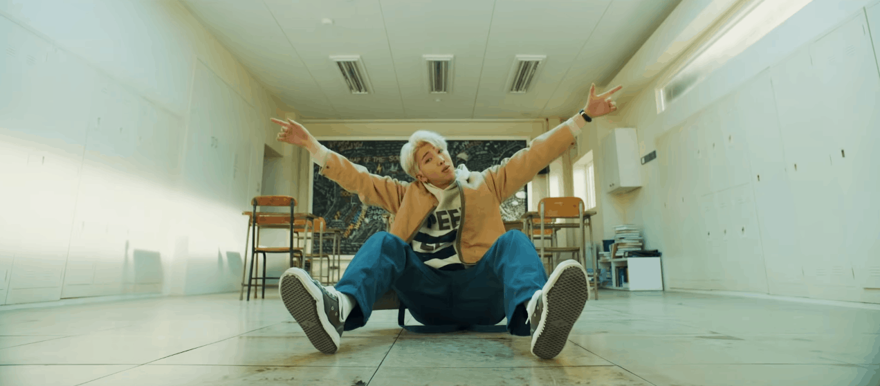 BTS Persona video screenshot - RM wearing jeans, sneakers, and a beige hoodie while sitting in a classroom