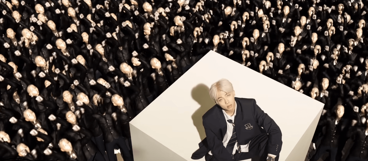 BTS persona video screenshot - RM in a black suit surrounded by clones