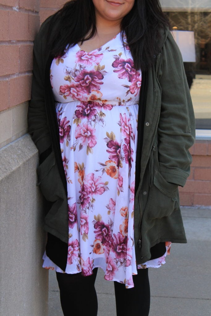 Katie wears a white and pink floral print sundress with a green jacket and black tights.