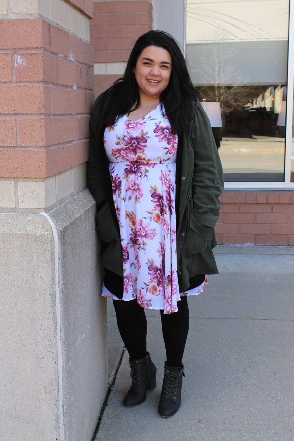Katie wears a floral print sundress with an olive green jacket, black tights, and grey chunky-heeled lace-up booties.