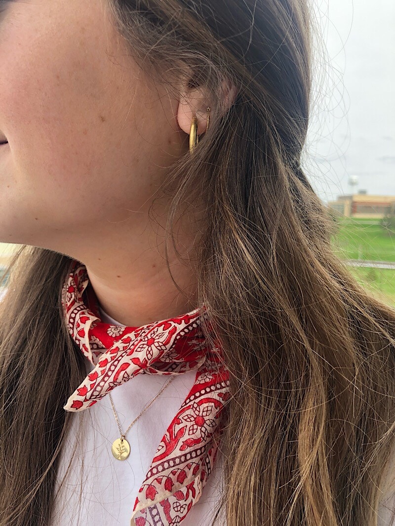 Ali wears gold Madewell hoops, a dainty GLDN pendant necklace, and a bright red bandana around her neck.