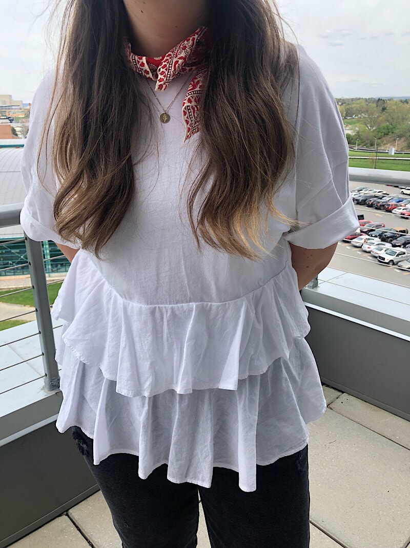 Ali wears a white short sleeve shirt with layered ruffles and cuffed sleeves.