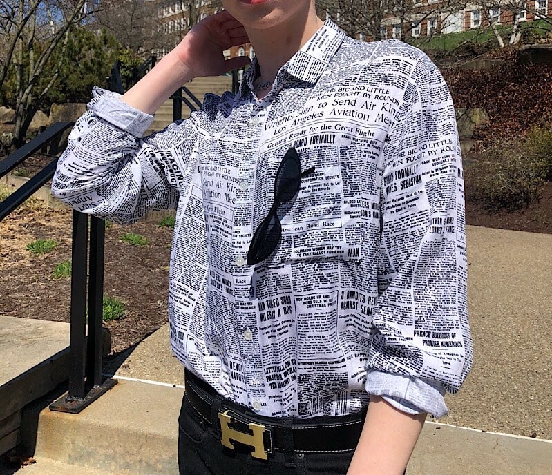 Caleb wears a button-up shirt in black and white newspaper print with an Hermes belt buckle.