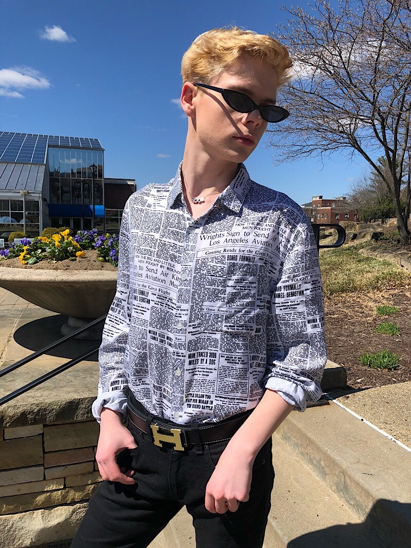 Caleb wears skinny black plastic framed sunglasses with his newspaper print button-up shirt and Hermes belt.