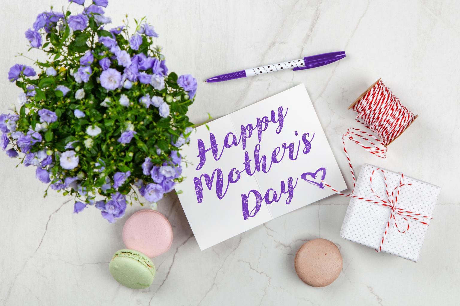 Flat lay on a pale gray marbled surface featuring purple flower plant, uncapped purple-and-white pen with a dotted design; white card that says 