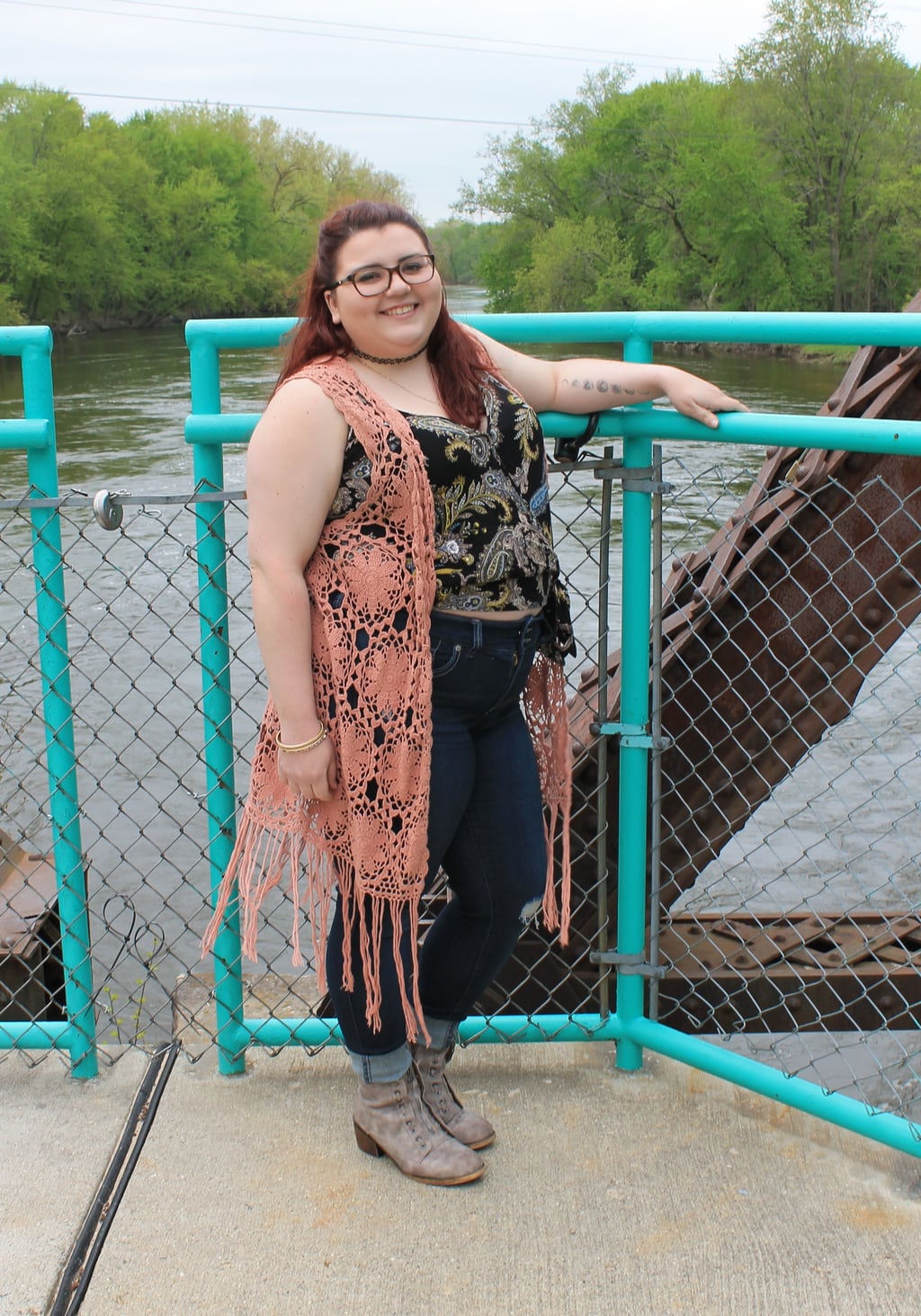 This Grand Valley State University student wears a coral crochet duster vest, a patterned black and gold wrap top, high-waisted skinny jeans, and grey booties.