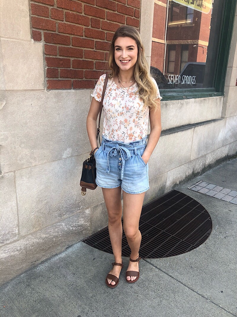 Savannah wears a simple patterned floral tee shirt with paper-bag ombre-wash denim shorts with a tied denim belt and simple brown sandals.