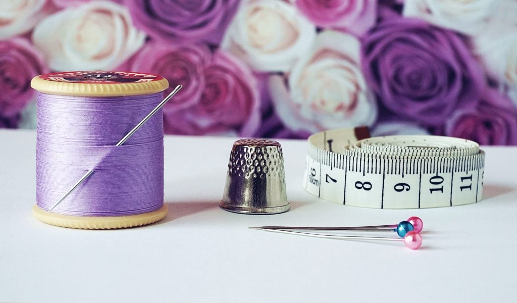 Bobbing of purple thread with needle, pins, and measuring tape