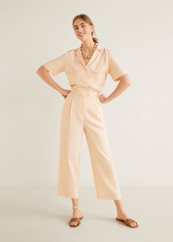 Woman wearing pale pink top tucked into matching cropped pale pink pants, flat sandals, and necklaces and anklet