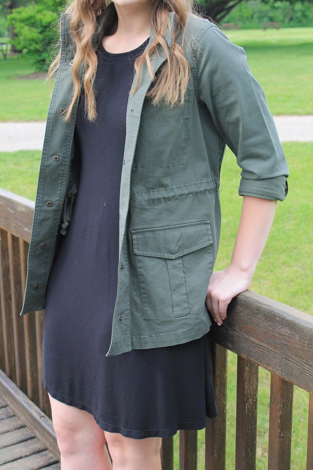 Rebecca wears a simple black shift dress with an army green anorak jacket.