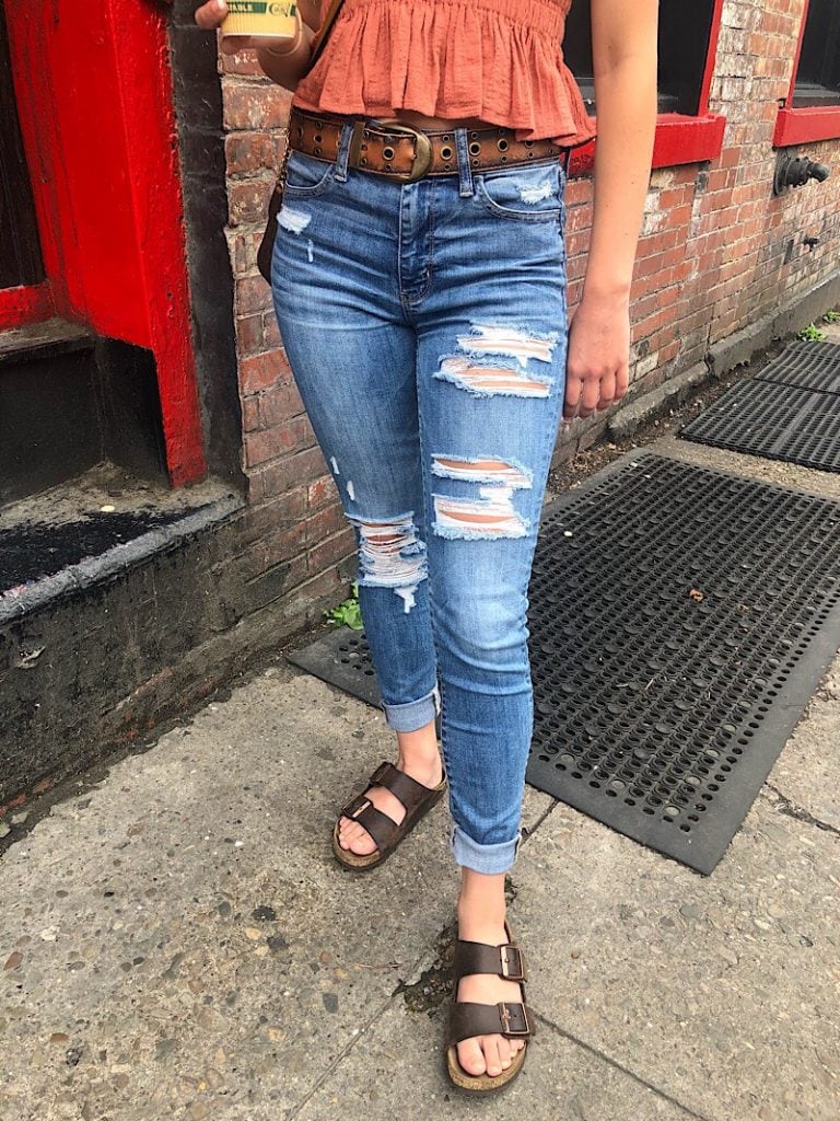 This West Virginia University student wears a pair of high-waisted medium-wash denim jeans with distressed legs and cuffed hems.