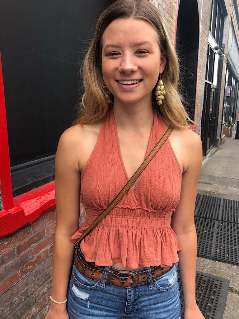 Logan wears a textured burnt orange halter top with a ruffle peplum.