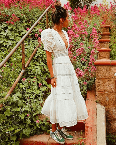 girl in longe white summer dress and green sneakers in front of a floral background