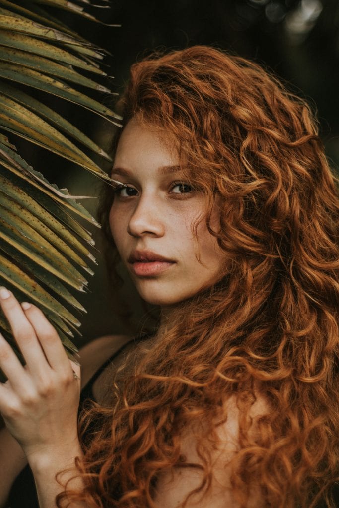 Close-up shot of woman with curly hair standing amongst leaves