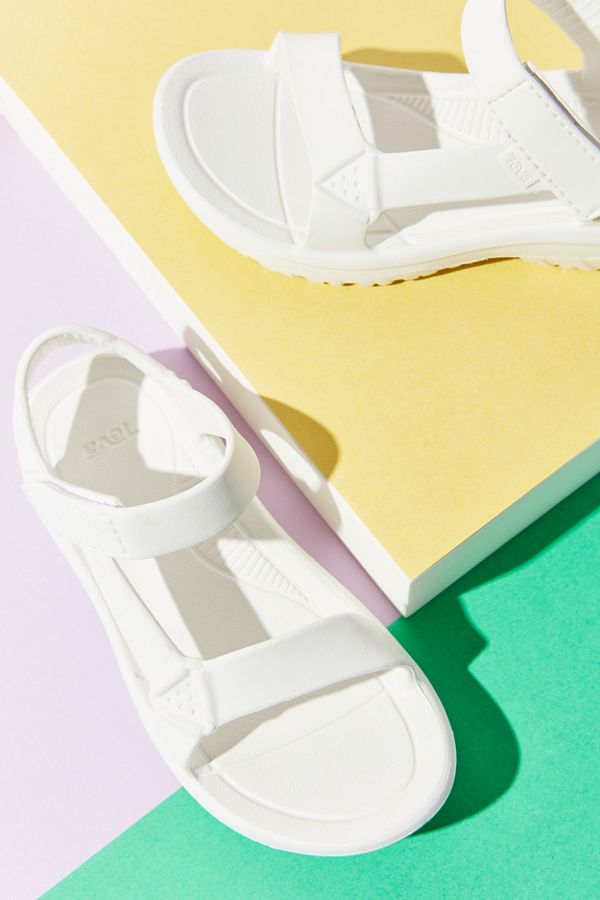 White rubber Teva sandals against a green and pastel yellow and lilac-colored background.