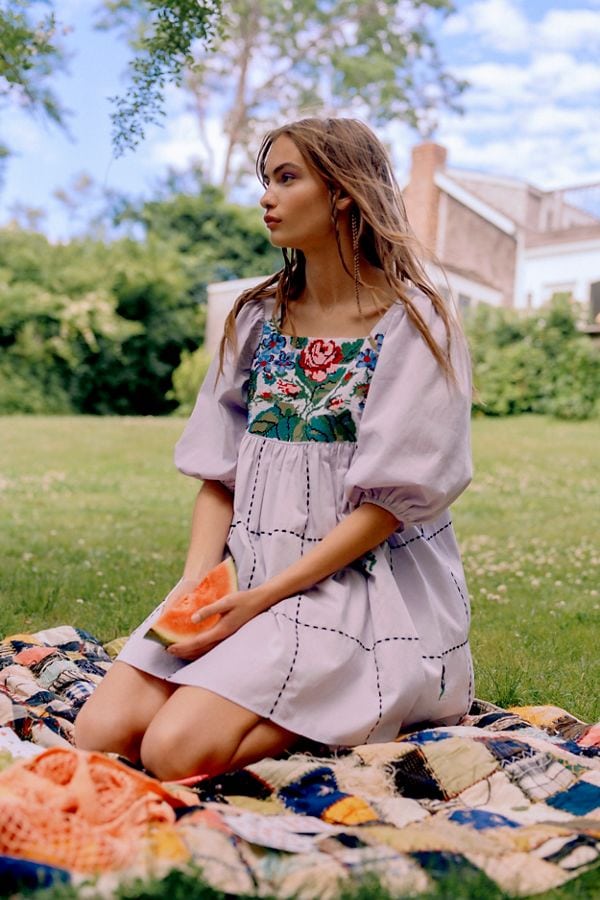 Woman wearing embroidered puff sleeve dress sitting outside on blanket and holding watermelon slice