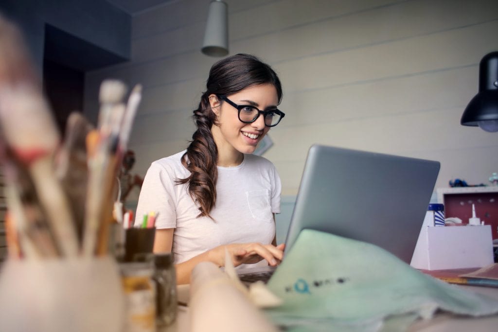 Girl on laptop surrounded by art supplies